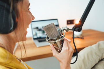 Woman sits on the table and recording podcast at his small cozy radio studio. Female podcaster...