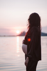 Beautiful woman in rays of dawn. Silhouette in profile of pregnant woman with hair flowing in wind...