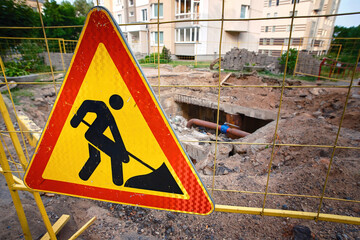 Earthwork sign on fence with trench hole in background, replace water pipes, heating main repair and renovation. Repair of city communications. Danger, deep excavation sign