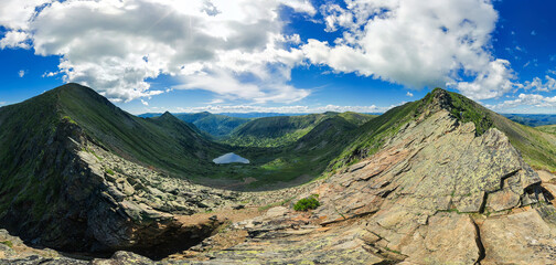 Landscape lake in the shape of a heart among high green mountains view from the cliff, sunny summer day and cloudy sky. Spherical panorama 360vr