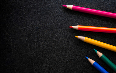 Bright colored pencils on a dark black background. Seven colors of the rainbow. Back to school. Education and creativity. Drawing and art. Free space for text.