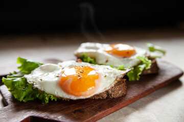 Closeup yummy toasts with fried eggs and lettuce leaves for breakfast placed on wooden board