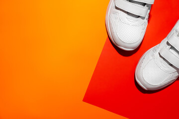 flat lay front parts of two white sneakers on a geometric paper orange and red background with copy...