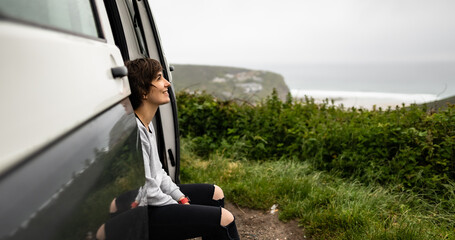 Attractive young female sitting inside a campervan while looking outside of the van and enjoying...