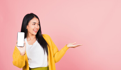 Happy Asian portrait beautiful cute young woman excited holding mobile phone blank screen presenting product with palm of hand at empty, studio shot isolated on pink background, female look to space