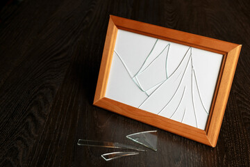 Brown photo frame with broken glass. Shards on a wooden table.