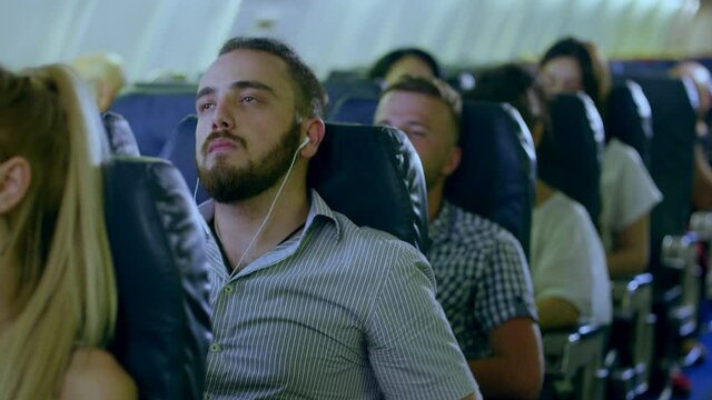 Young man in headphones listening to music and relaxing during fly in airplane . Man on commercial airplane listening to music on an MP3 player through noise cancelling headphones . Shot on RED camera