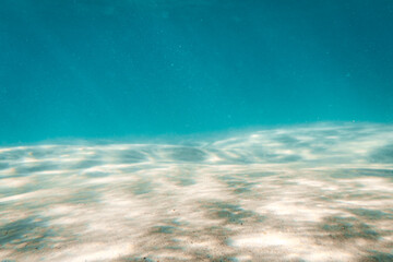 Fototapeta na wymiar Underwater Scene whit Sunbeams Coming Through the Water and Reflected on Sand Floor. Background