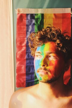 Closeup Portrait of young man face painted as lgbtq rainbow pride flag with sunset sunlight on face and curly hair *2