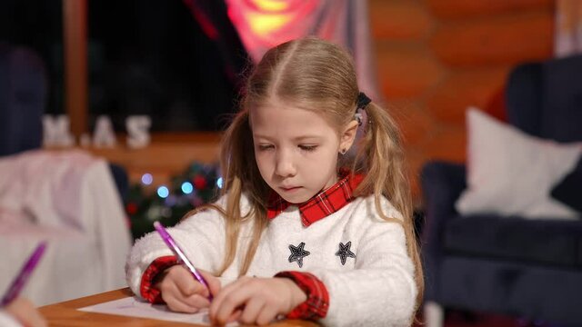 Portrait of a lovely little girl indoors at Christmas. Cute child writing a letter to Santa. Beautiful small girl drawing a picture on xmas background at home.