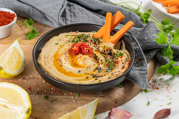 Delicious hummus in ceramic bow lwith  carrot stick dipped in hummus. Colorful snack composition on a white background.
