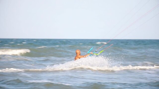 Young adult caucasian fit male person enjoy riding kite surf board macking extreme trick stunt bright sunny day against blue sky at sea or ocean shore. Watersport adrenaline fun adventure acitivity