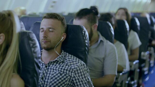 Young man in headphones listening to music and relaxing during fly in airplane . Man on commercial airplane listening to music on an MP3 player through noise cancelling headphones . Shot on RED camera
