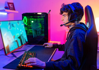 Fototapeta premium Caucasian young man in his room with colorful background plays video games on computer as hobby, entertainment and fun
