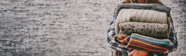 woman holding in hands Stack of cozy knitted sweaters on gray wall background