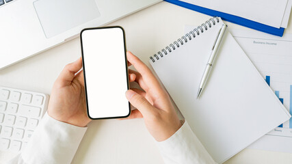 Accountant holding white screen cell phone with pen and notebook, calculator and laptop on office desk.