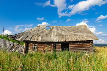 Fototapeta na wymiar Old wooden rustic ruined abandoned house against a blue sky with white clouds on a bright summer sunny day. Close-up. Scenery