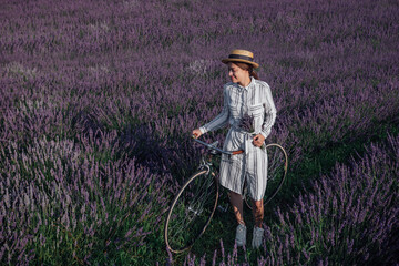 Young woman with retro bicycle and lavender bouquet on violet flowers field background