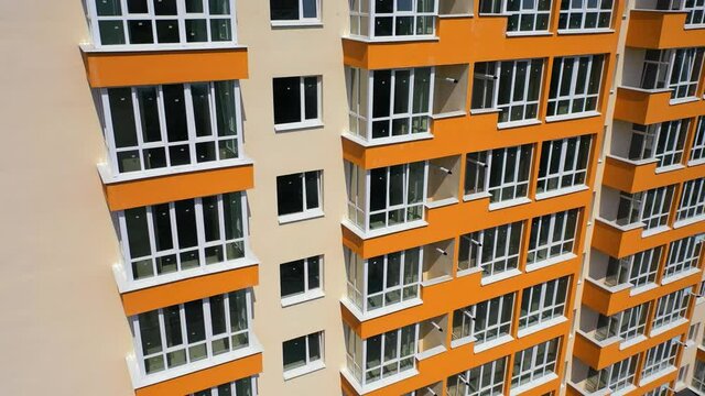 Building exterior of city multi-story apartment building. Facade of skyscraper building with new plastic windows and orange balconies at sunshine.