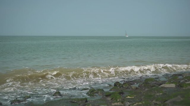 Waves on the coast with a sailing ship in the background, slow motion.