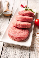Plate with raw cutlets made of fresh forcemeat on light wooden background