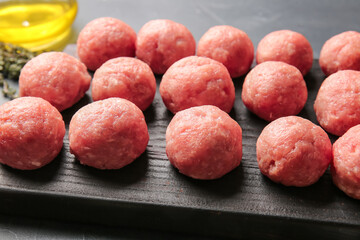 Wooden board with raw cutlets made of fresh forcemeat on dark background, closeup