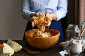 Woman preparing tasty sauerkraut at table in kitchen, closeup