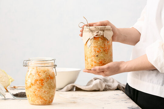 Woman with glass jar of tasty sauerkraut at table in kitchen