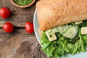Plate with tasty sandwich, sauce pesto, cucumber and cheese on wooden background, closeup