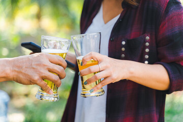 Cropped shot of people holding beer glasses celebrating in the summer camping party outdoor. Friends clinking bottle of beer during camping outdoor