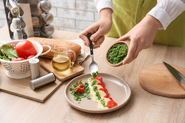 Woman preparing caprese salad with pesto sauce in kitchen