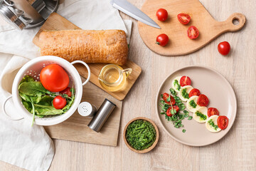 Plate with tasty caprese salad and ingredients on wooden background