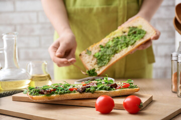 Woman preparing tasty sandwich with pesto sauce in kitchen