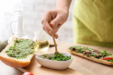 Woman preparing tasty sandwich with pesto sauce in kitchen, closeup