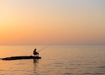 Naklejka premium Fisherman silhouetted against a dusk sky