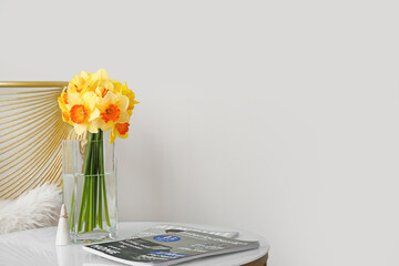 Vase with beautiful daffodils and magazines on table in room