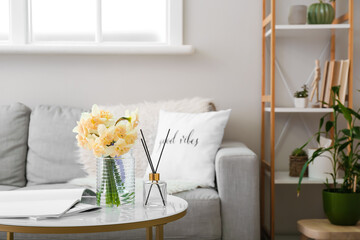 Vase with beautiful daffodils and reed diffuser on table in room