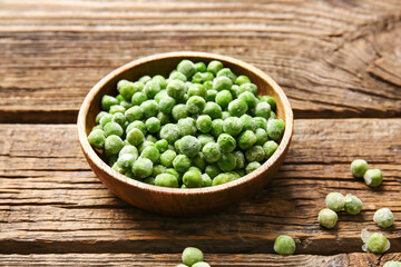 Bowl with frozen green peas on wooden background