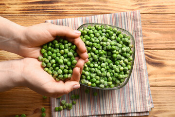 Female hands with frozen green peas on wooden background