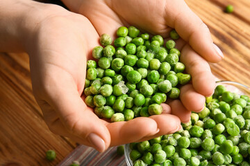 Female hands with frozen green peas on wooden background