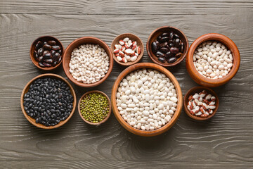 Bowls with different legumes on dark wooden background