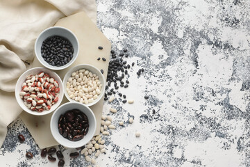 Bowls with different types of beans on grunge background