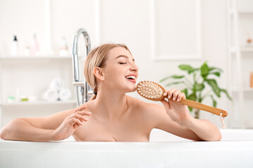 Beautiful young woman with massage brush singing in bathroom