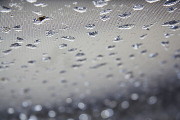 Raindrops on black mesh fabric. Plenty of small water drops on it. Blurred background with sparkle of lights
