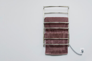 Electric heated towel rail in the bathroom against the background of a gray wall.