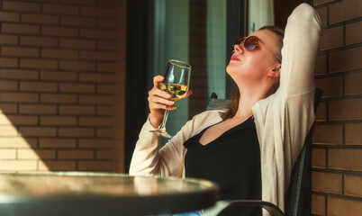 Woman in sunglasses enjoying white wine on the balcony.