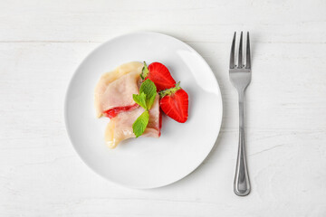 Plate with tasty strawberry dumplings on light wooden background