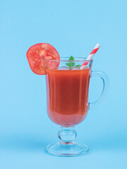 Fresh tomato juice in a glass glass on a leg on a blue background.