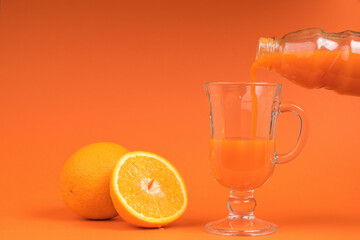 Orange smoothie is poured from a bottle into a glass glass on an orange background.