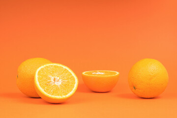 Whole and sliced oranges on an orange background.